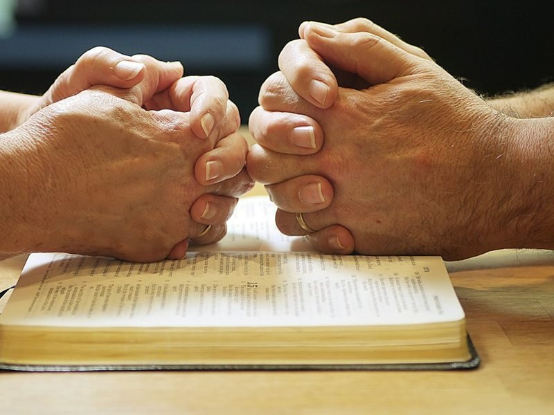 Des mains jointes posées sur une Bible ouverte
